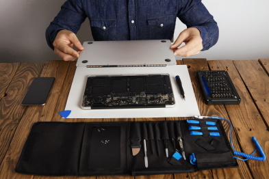 service-man-opens-backside-topcase-cover-of-computer-laptop-before-repairing-cleaning-and-fixing-it-with-his-professional-tools-from-toolkit-box-near-on-woode